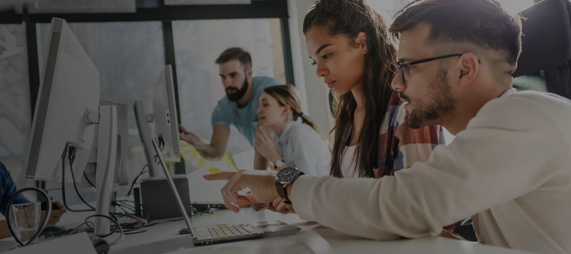 Equipe de jovens profissionais colaborando em frente a computadores em um escritório moderno.