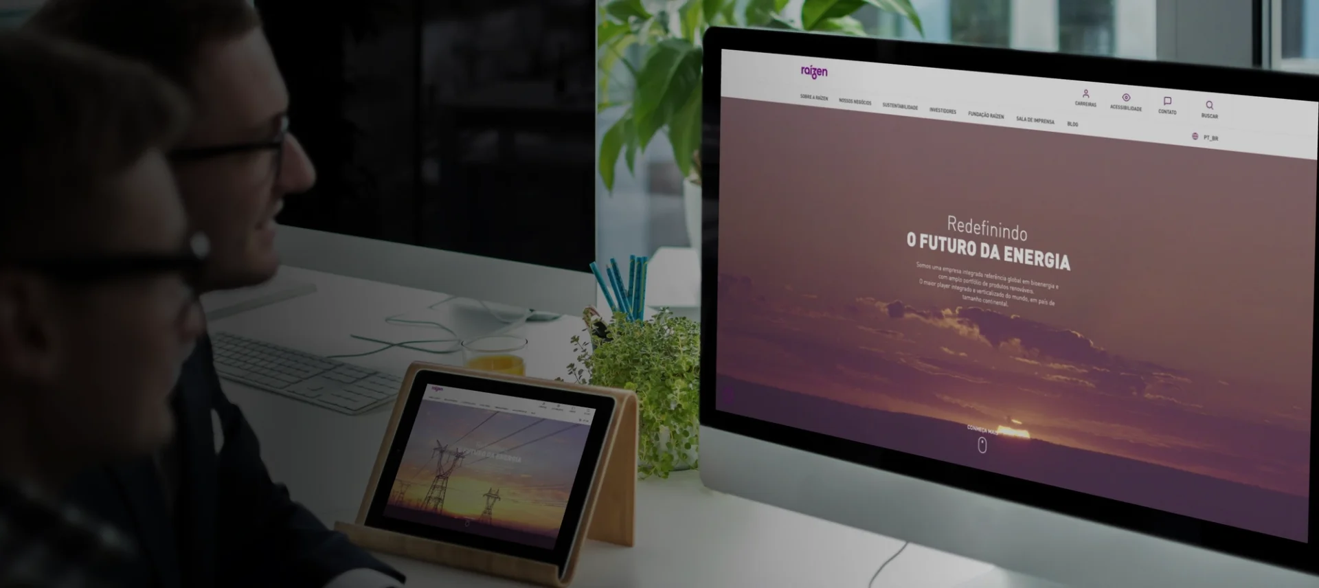 Dois homens olhando para um monitor e um tablet, ambos mostrando a tela de um site sobre energia